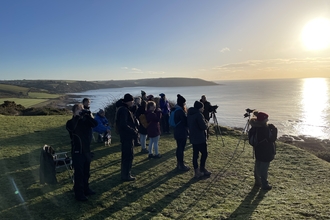 A group of people on a calm morning looking out to sea with telescopes.