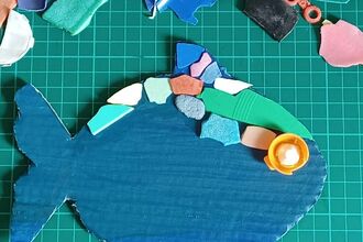 A fish made using coloured bits of paper on a green background