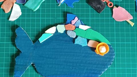 A fish made using coloured bits of paper on a green background